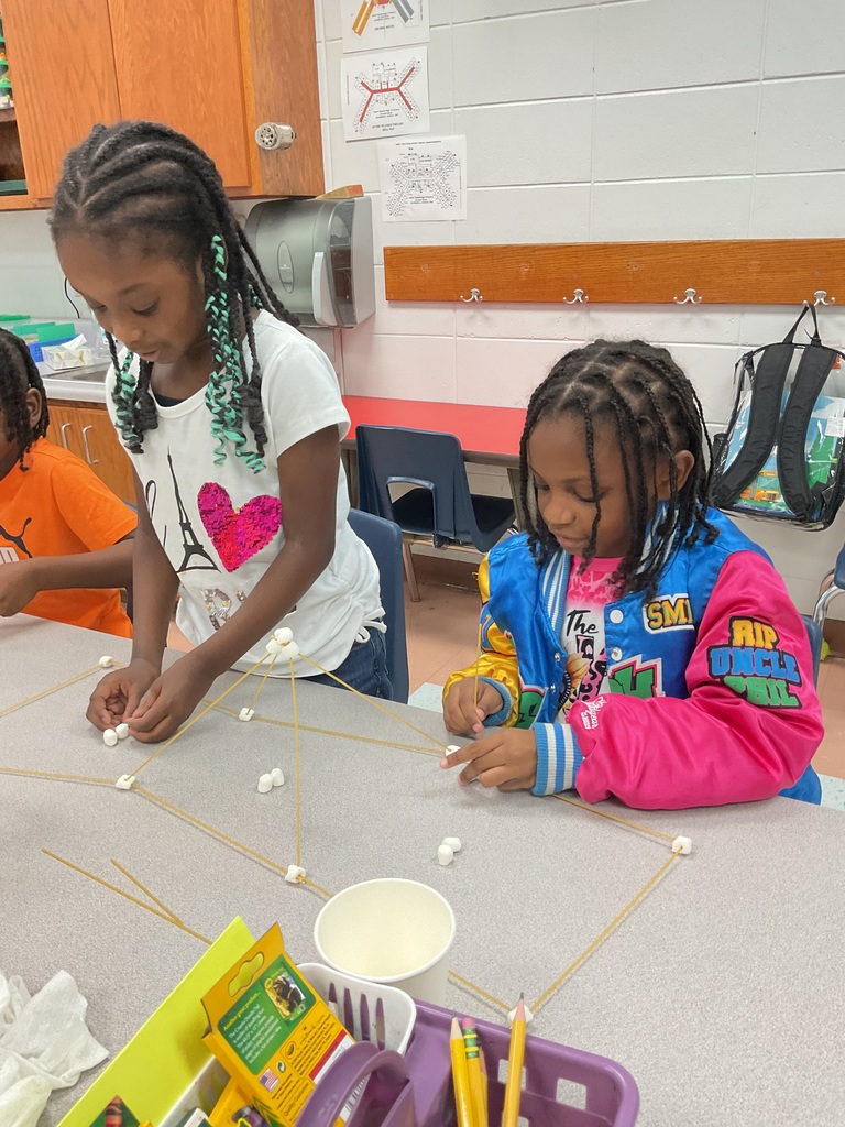 Two girls construct spaghetti and marshmallow structures during a STEM classroom activity.