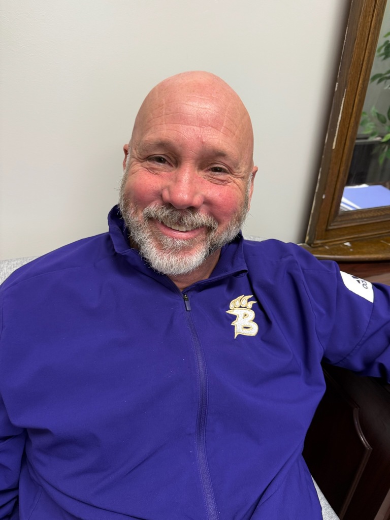 Portrait of an individual wearing spirited purple and gold Bearcat attire. The background varies, including office and home settings with decorative and school-related items visible.