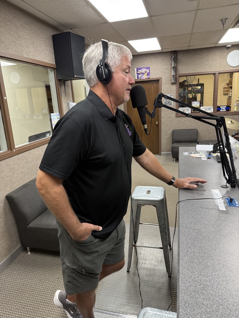 Coach Jay Walls speaks into a microphone wearing headphones inside a radio studio.