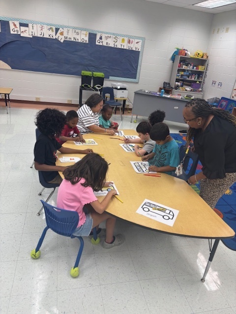 Teachers and students sitting at a table doing art projects.