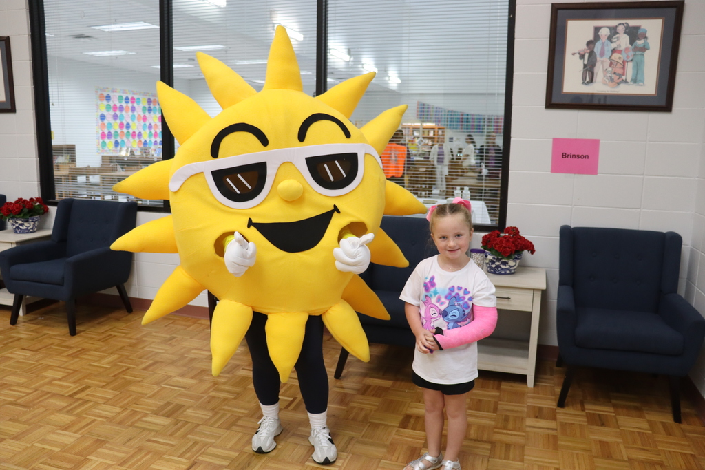 A student with a pink cast smiles for a photo next to Sunny the SunStop mascot, who poses playfully with finger guns.