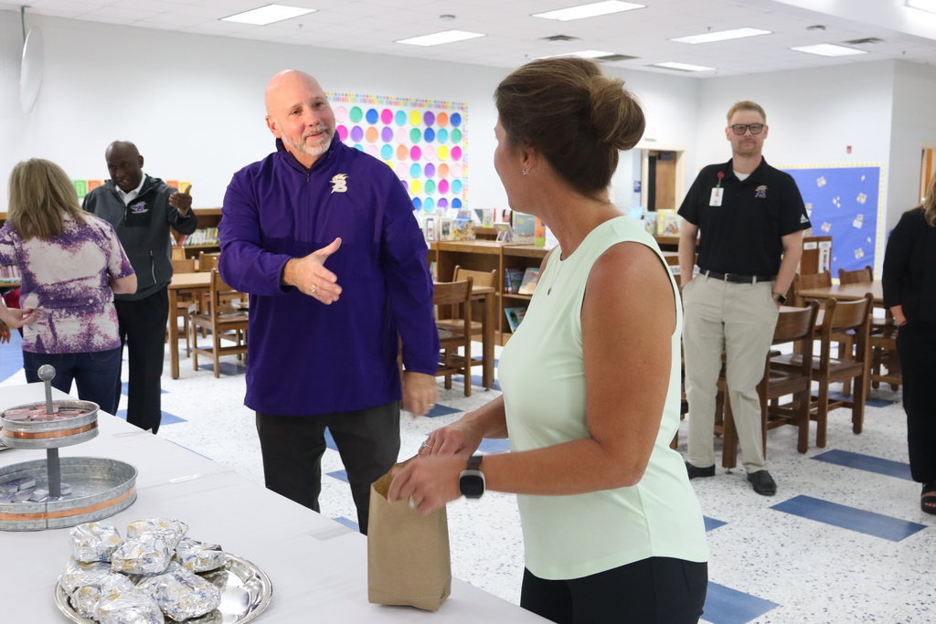 Superintendent Dr. Boyd English greets an educator with a handshake while staff and administrators mingle around the breakfast table filled with biscuits.