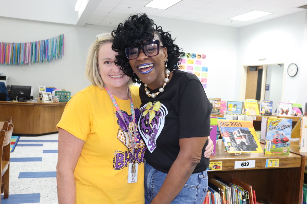 Two educators embrace and smile for the camera during the “Biscuits for the Best” appreciation breakfast inside the school library.