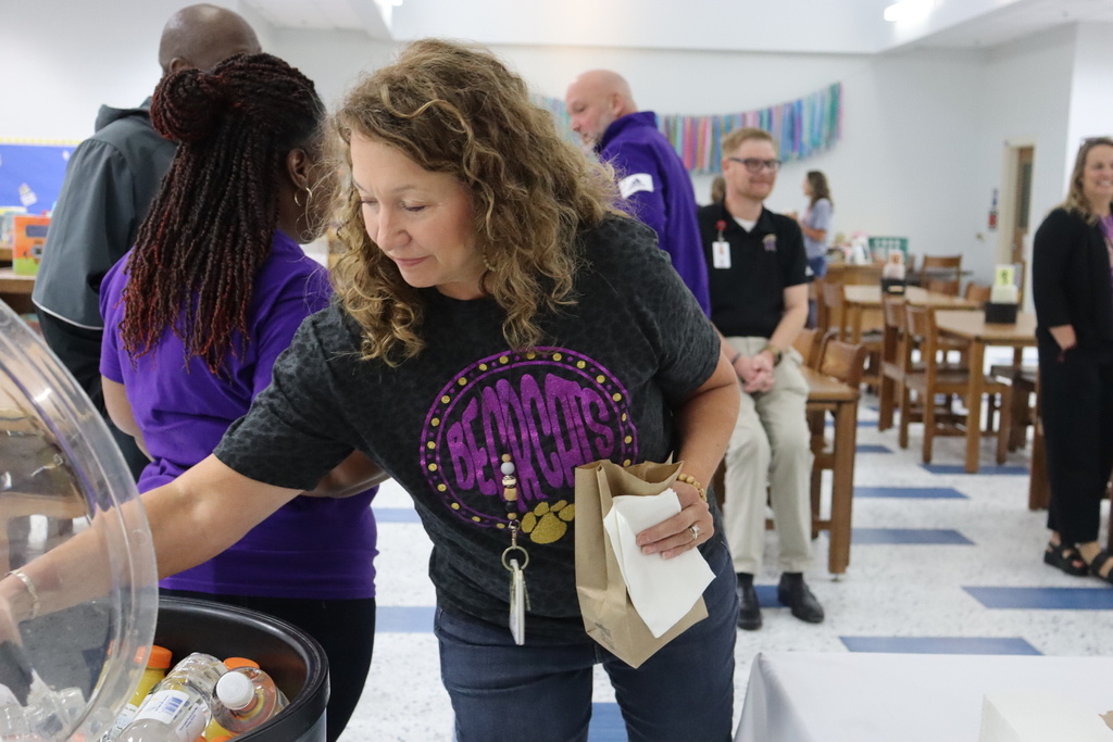 A teacher in a Bearcats shirt selects a drink from a cooler while holding a paper bag with her breakfast.