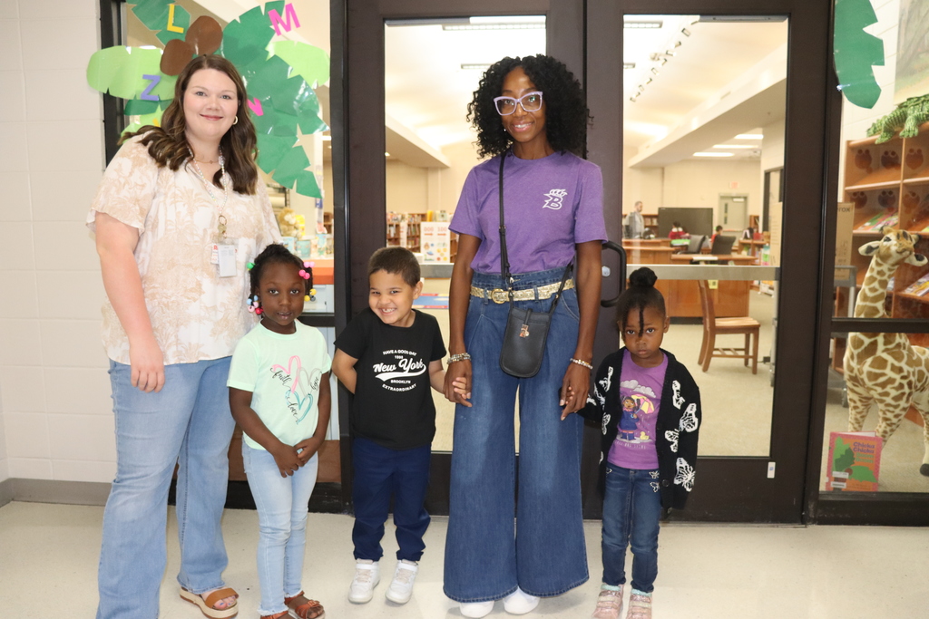 A woman stands with three young children in front of the media center doors, smiling together before heading inside.