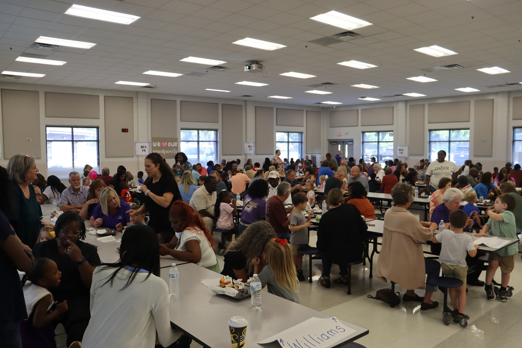 A wide view of the school cafeteria filled with grandparents, students, and staff enjoying breakfast together during the event.