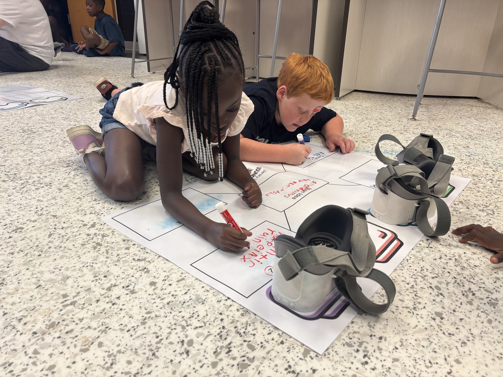 This image contains kids writing on a poster and looking inside of the VR Headsets.