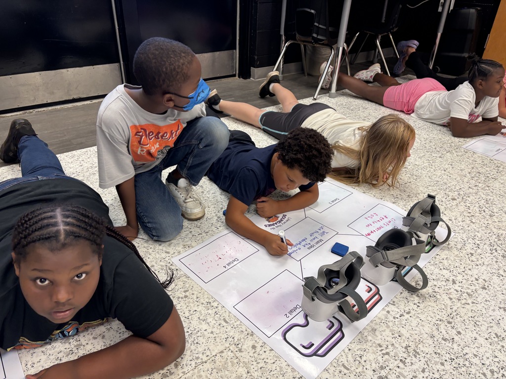 This image contains kids writing on a poster and looking inside of the VR Headsets.