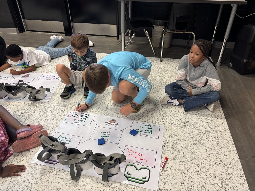 This image contains kids writing on a poster and looking inside of the VR Headsets.