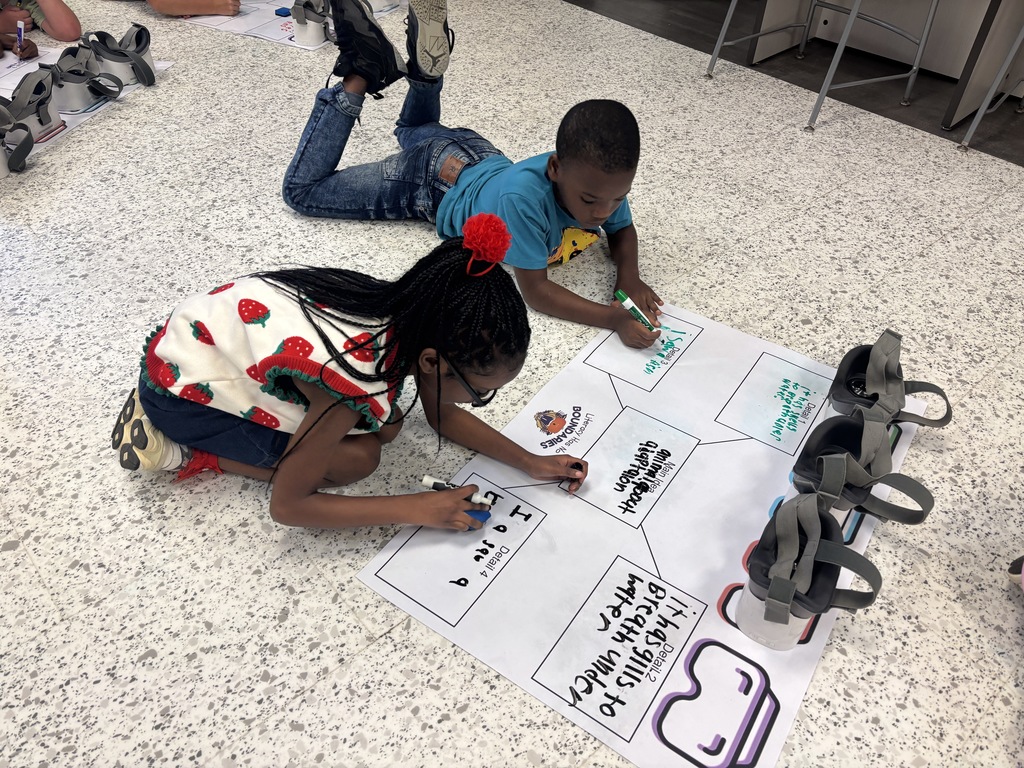 This image contains kids writing on a poster and looking inside of the VR Headsets.