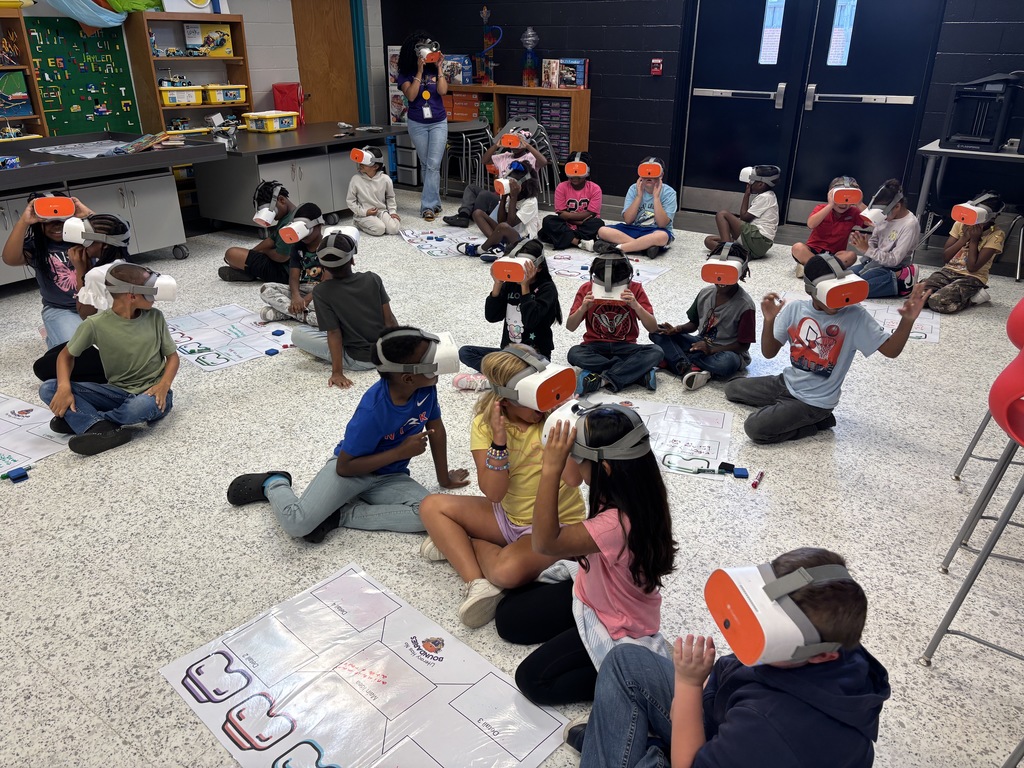 This image contains kids writing on a poster and looking inside of the VR Headsets.