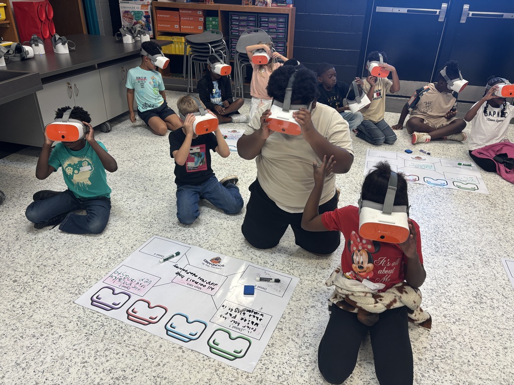 This image contains kids writing on a poster and looking inside of the VR Headsets.