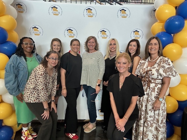 Group of women posing in front of a GACIS backdrop with blue, yellow, and white balloon columns