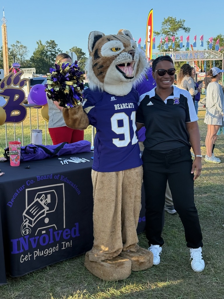 parent and familiy engagement director stands hugging buddy the bearcat mascot infront of vendor table at the fair