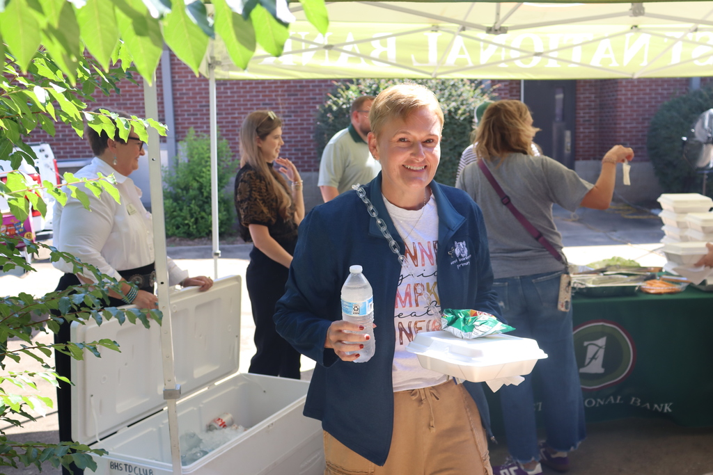 women smiles while holding a to go plate and water bottle