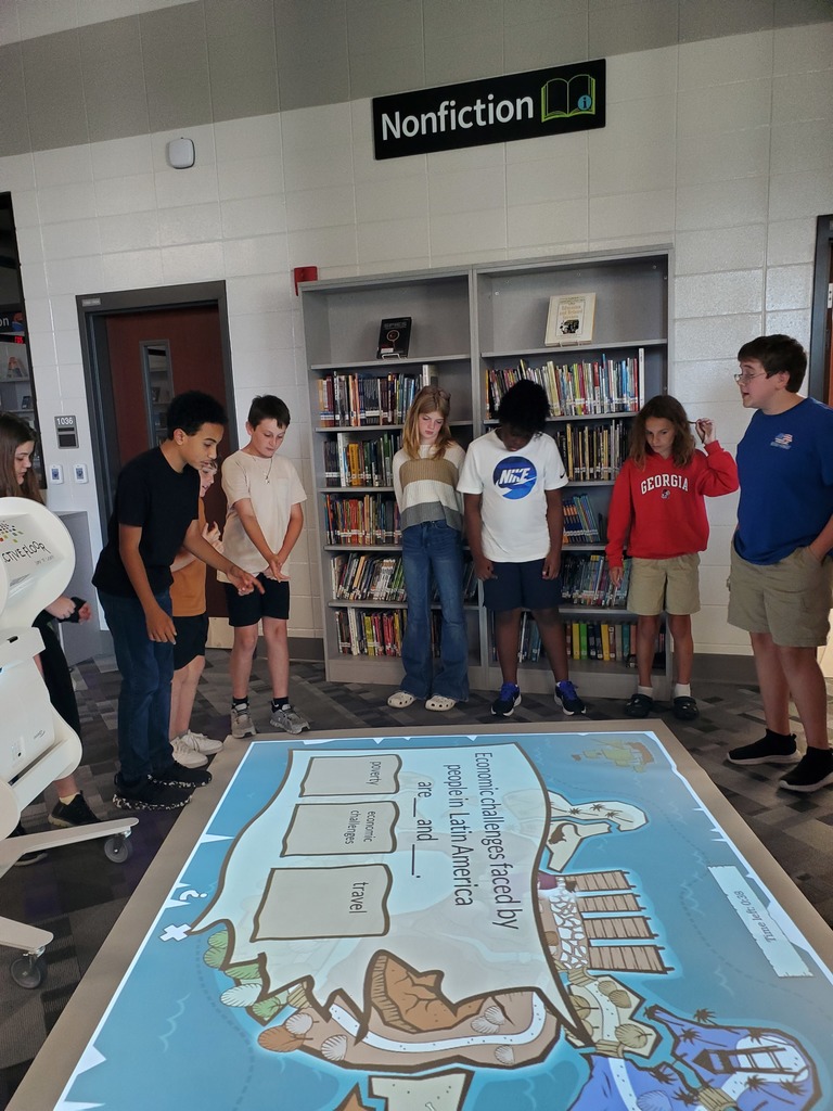 Group of students standing in a library around an interactive floor projection displaying a question on Latin America’s economic challenges