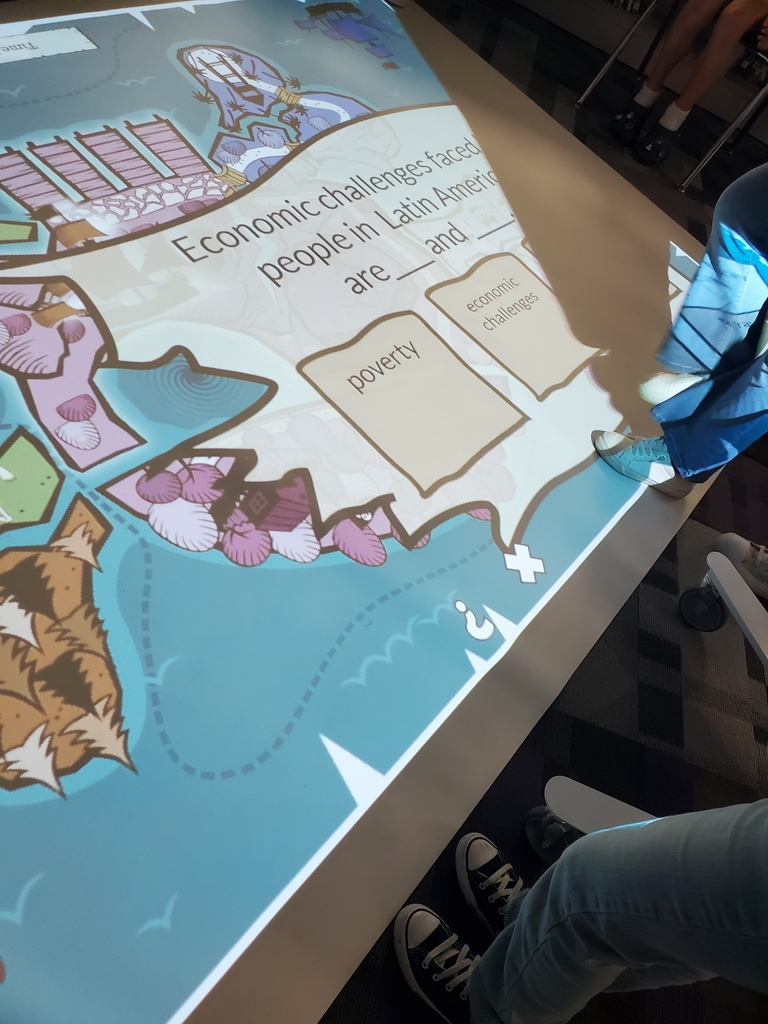 Interactive floor projection showing a question about economic challenges in Latin America with students’ feet visible around the display