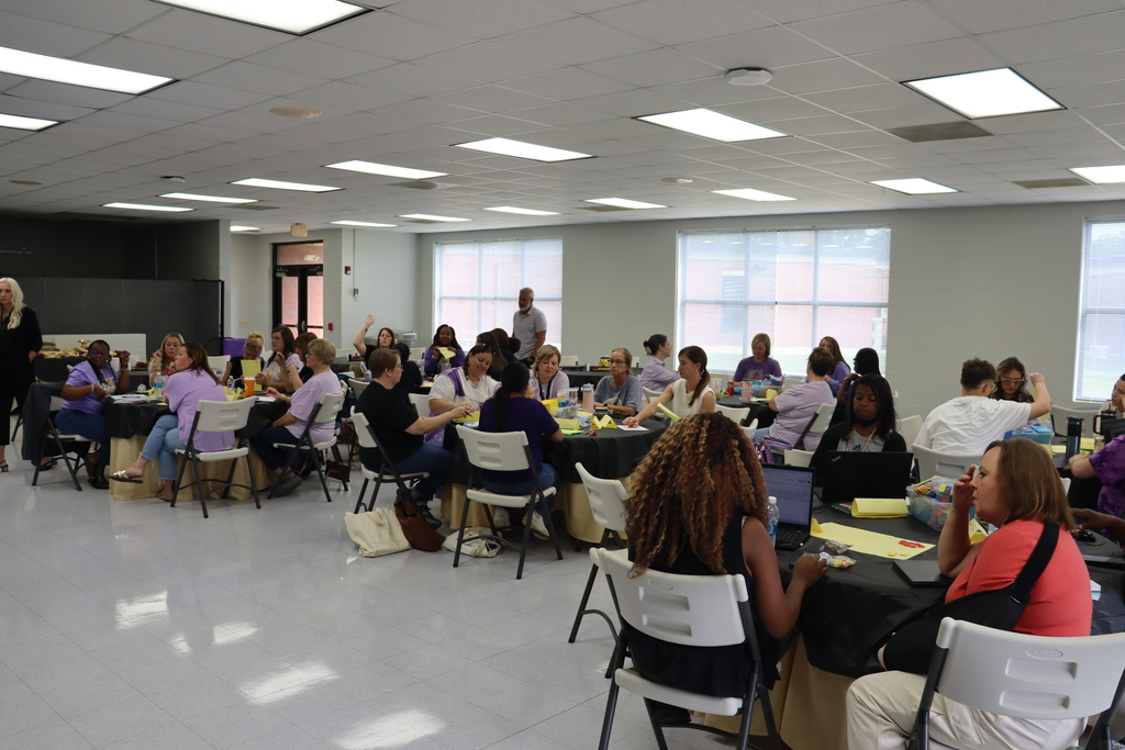 Large group of educators seated at tables engaged in discussion during a professional learning workshop.