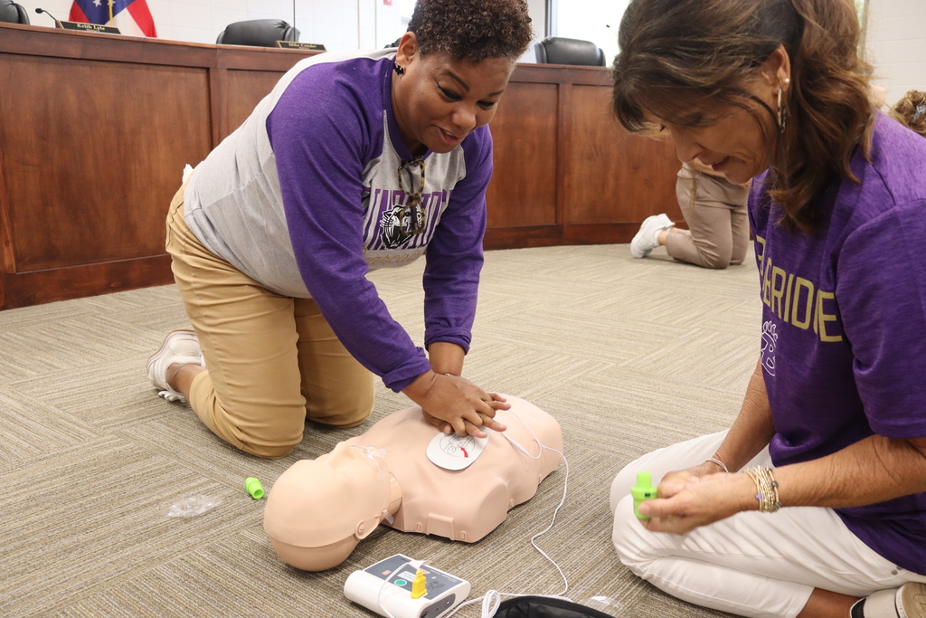 Two teachers performing CPR compressions on a training mannequin during a safety workshop.