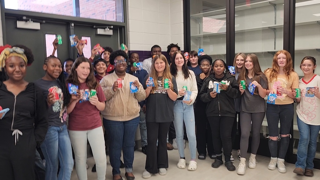 a group of students gather excitedly for a picture holding a snack and soda in a school hallway