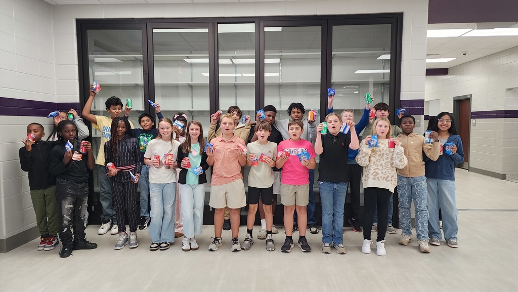 a group of students gather excitedly for a picture holding a snack and soda in a school hallway