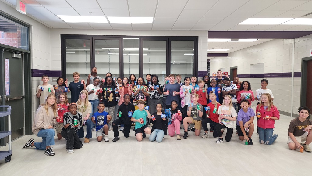 a group of students gather excitedly for a picture holding a snack and soda in a school hallway