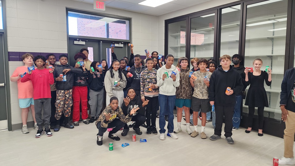 a group of students gather excitedly for a picture holding a snack and soda in a school hallway