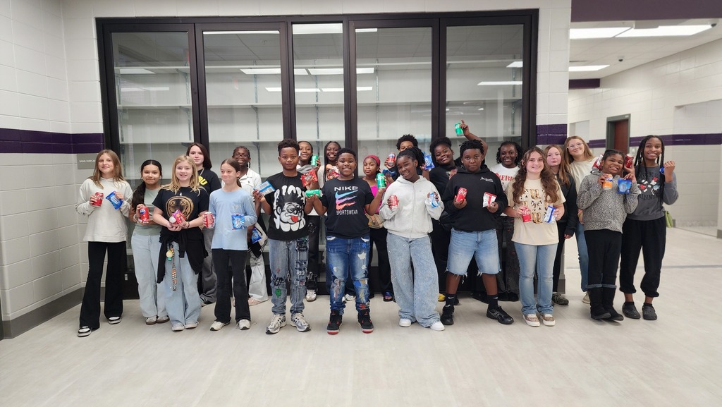 a group of students gather excitedly for a picture holding a snack and soda in a school hallway