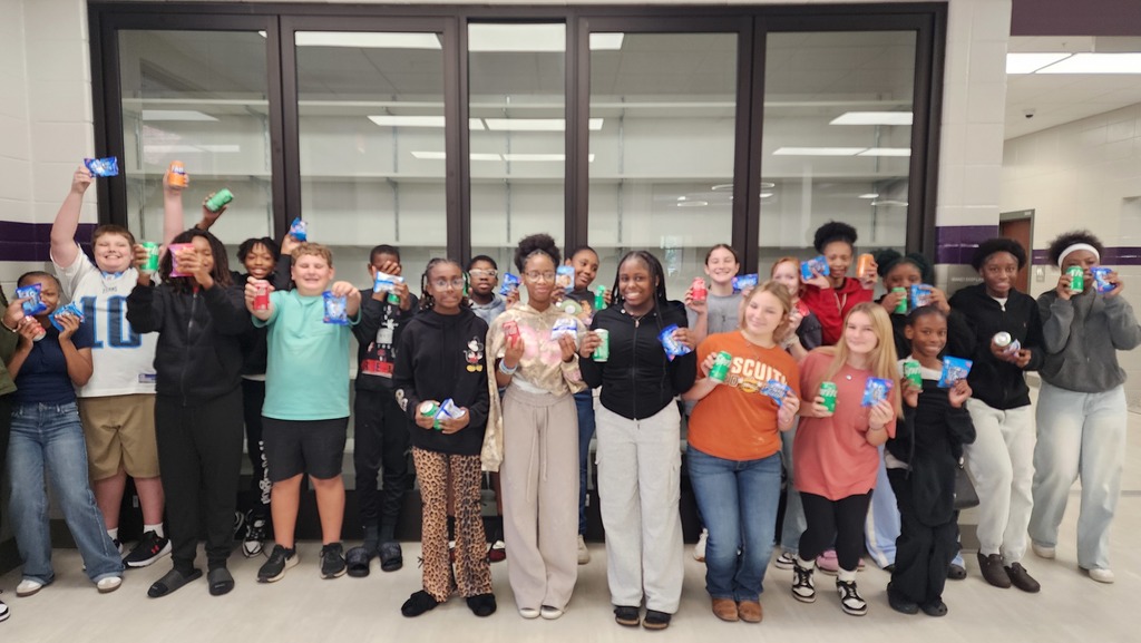a group of students gather excitedly for a picture holding a snack and soda in a school hallway