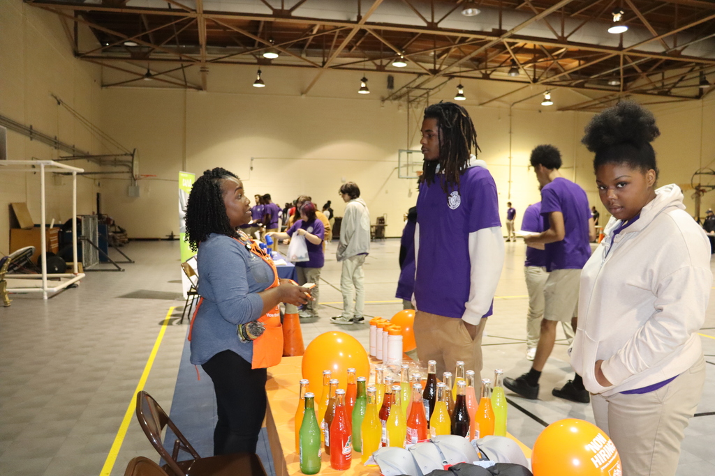 A Home Depot representative talks with two students at a career fair while others explore booths in the background.