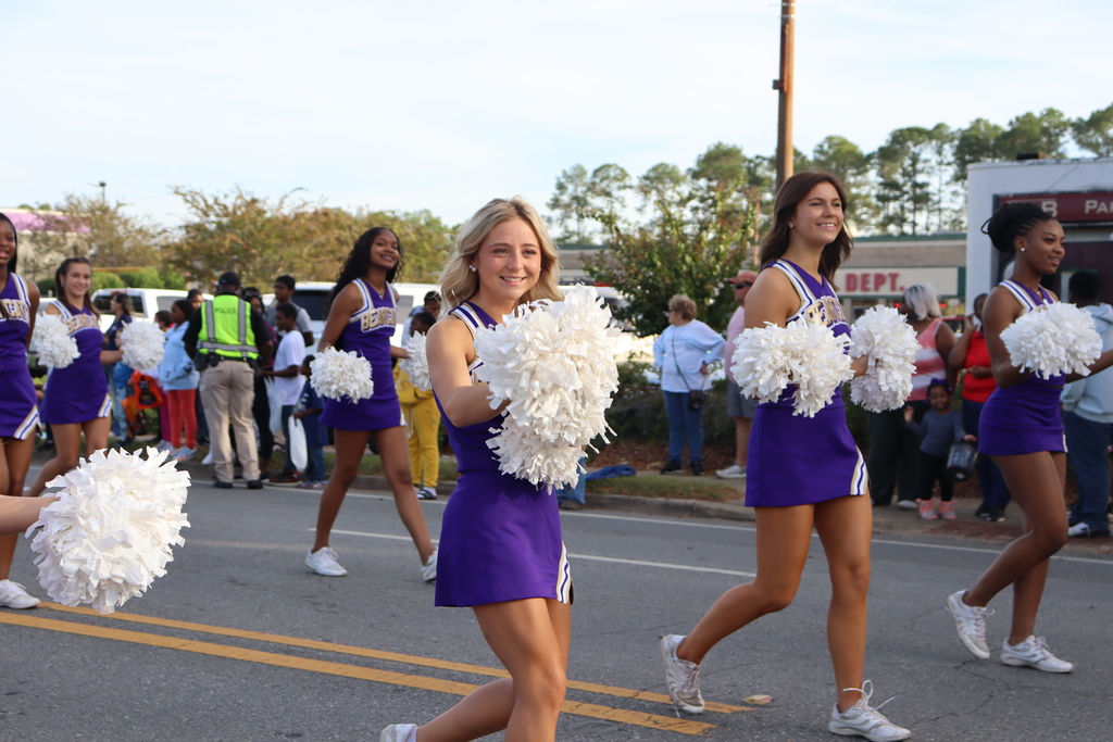 Bainbridge High School cheerleaders march in formation during a community parade, smiling and waving pom-poms.