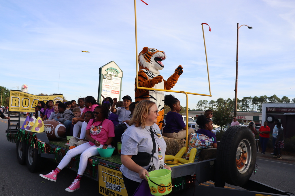 Hutto Elementary School parade float features students, staff, and a tiger mascot waving to the crowd.