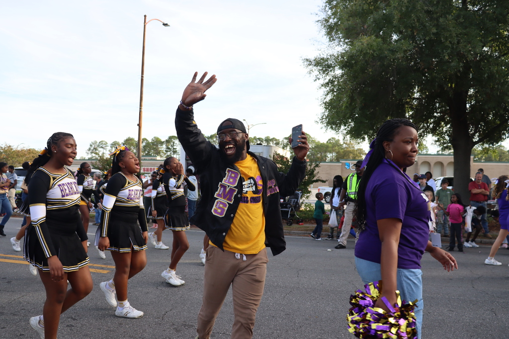 Bainbridge Middle School cheerleaders march with their coach, who waves enthusiastically to the crowd.