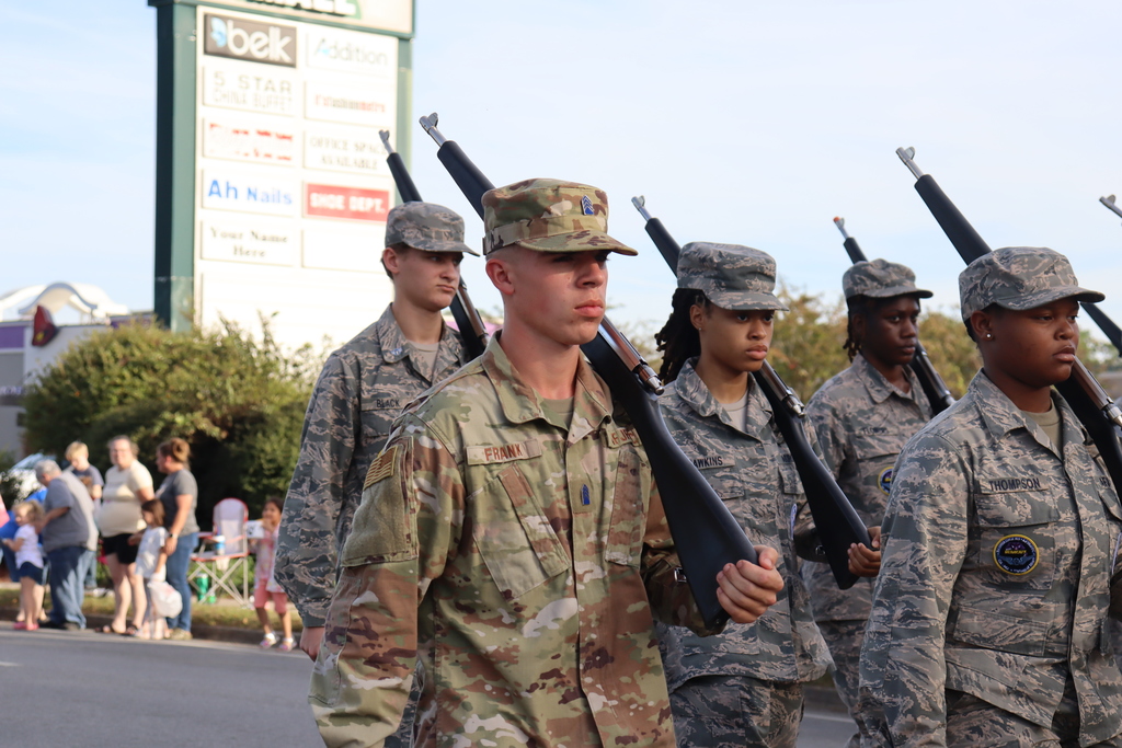 Bainbridge High School JROTC cadets march in uniform, carrying rifles in precise formation.