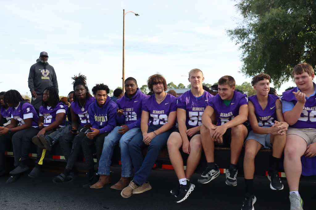 Bainbridge High School football players ride on a parade float wearing purple jerseys and smiling at the crowd.