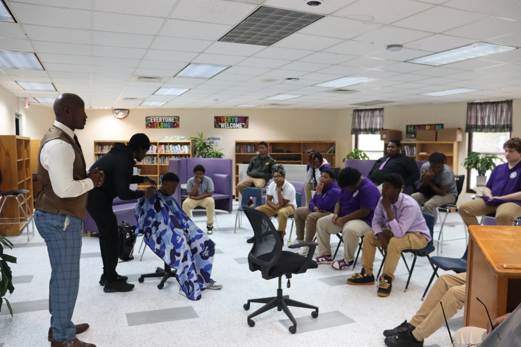 A barber gives a student a haircut as others watch and listen during the Cuts and Convos session.