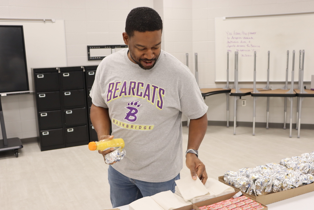 A Bainbridge Middle School staff member wearing a Bearcats shirt picks up a breakfast biscuit and orange juice during Biscuits for the Best.