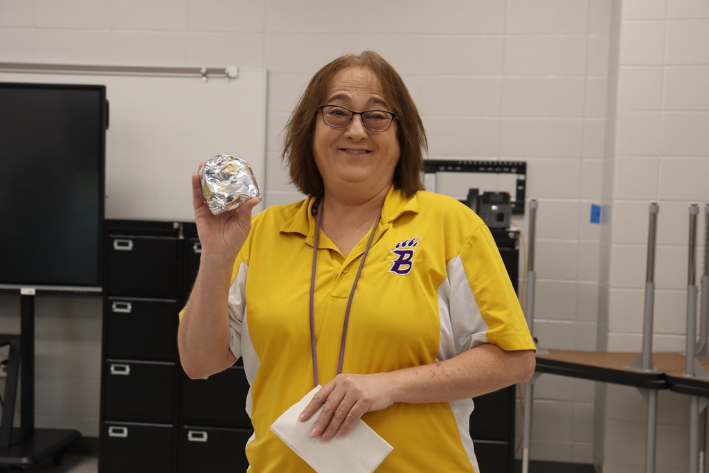 A smiling BMS staff member in a gold Bearcats shirt holds up her breakfast biscuit.