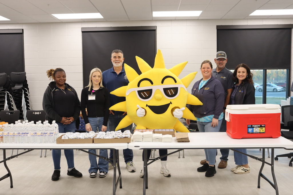 Sunny the SunStop mascot poses with SunStop team members behind a table of breakfast biscuits and drinks.