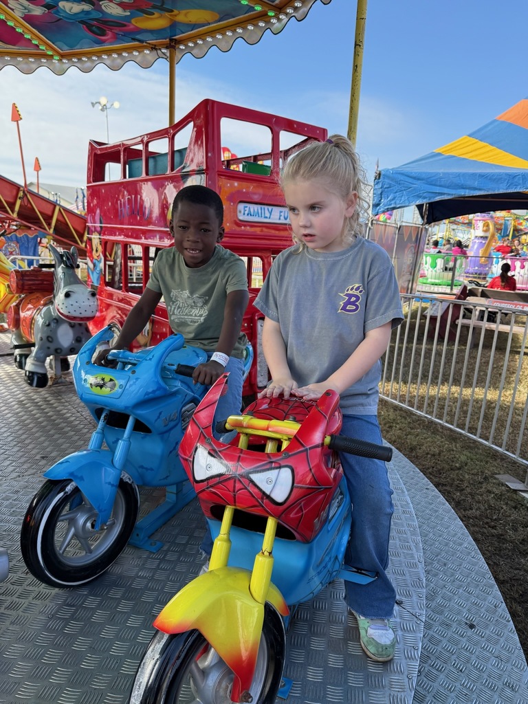 Two children ride colorful toy motorcycles at a carnival, smiling and enjoying the fun.