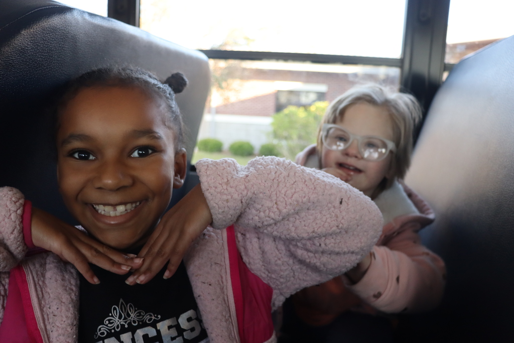 Two smiling children sit together on a bus, enjoying the ride.