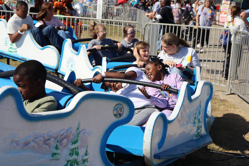 Children laugh and enjoy a fast-moving blue carnival ride on a sunny day.