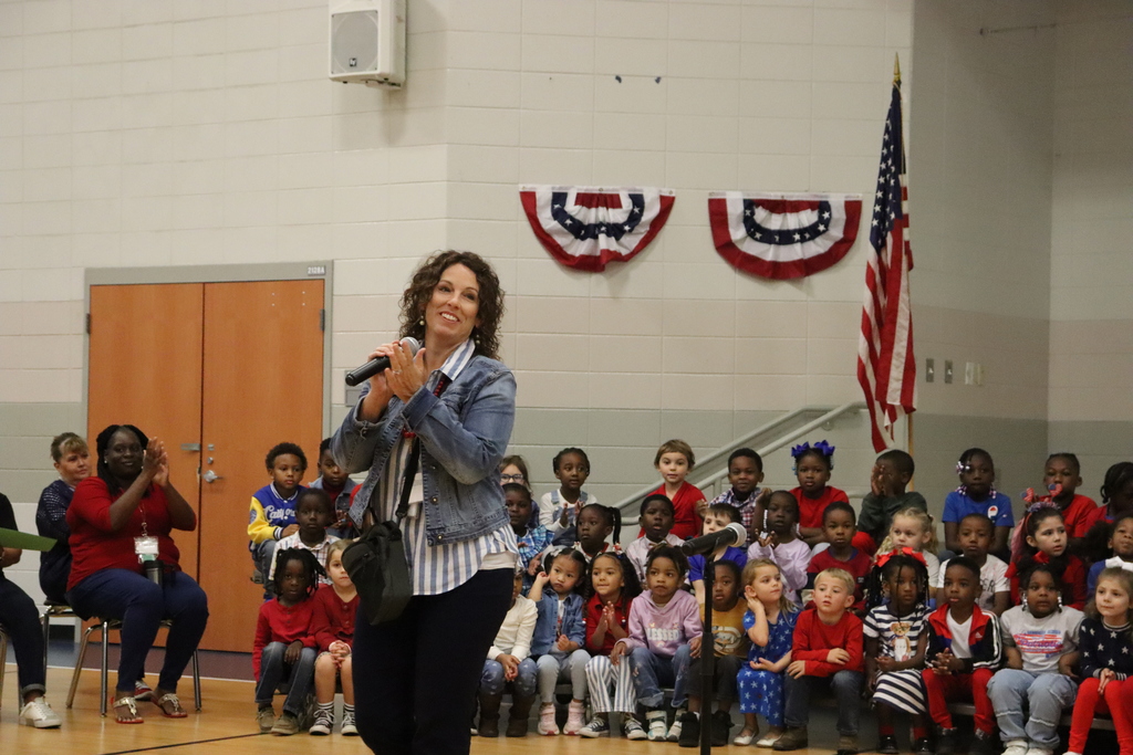 A woman stands in front of the JWP kindergarten choir, smiling and clapping during the program.