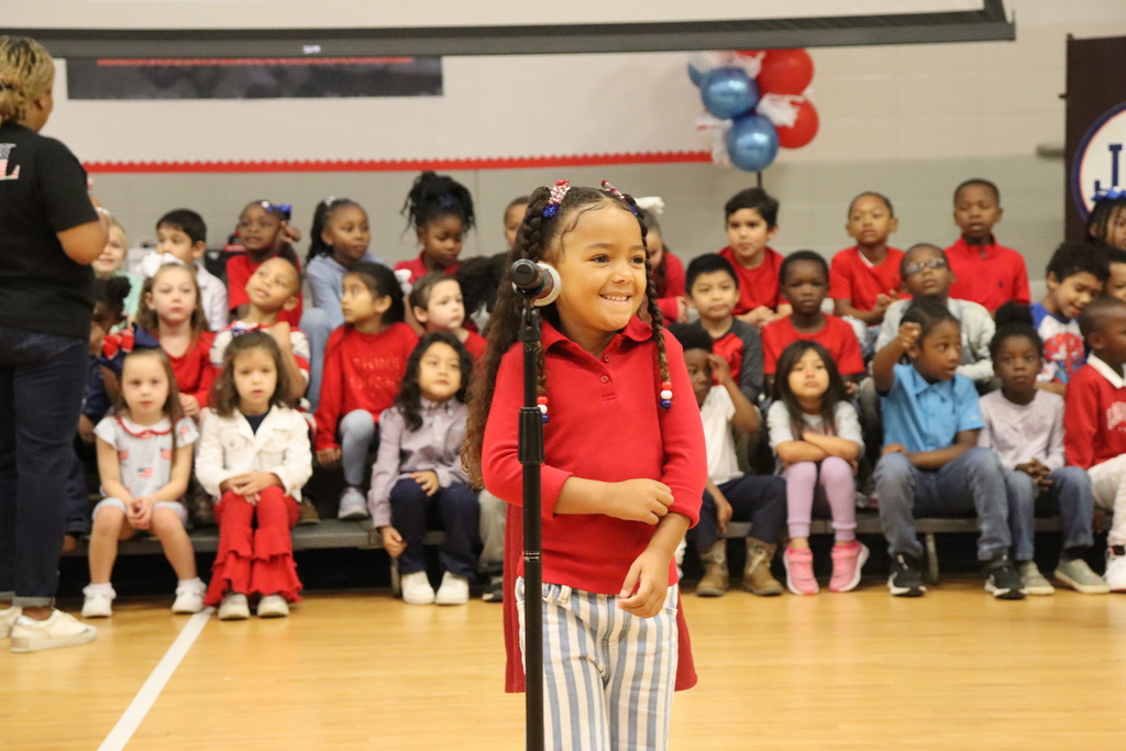A young girl smiles as she stands at the microphone during the kindergarten Veterans Day program.
