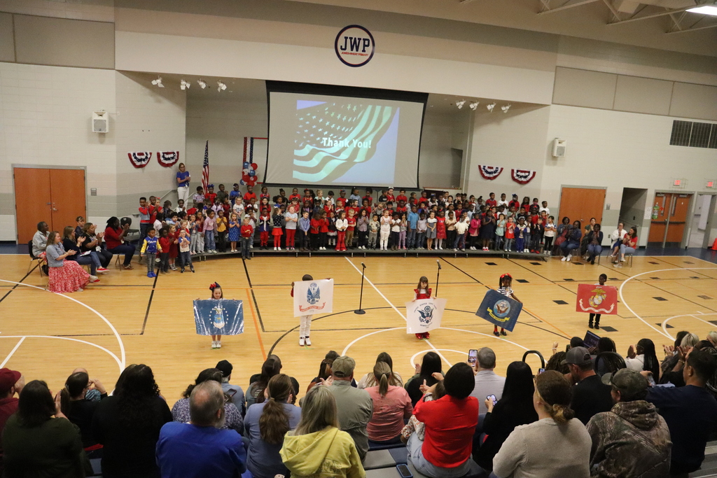 Wide shot of the JWP gym showing students performing on stage while the audience watches.