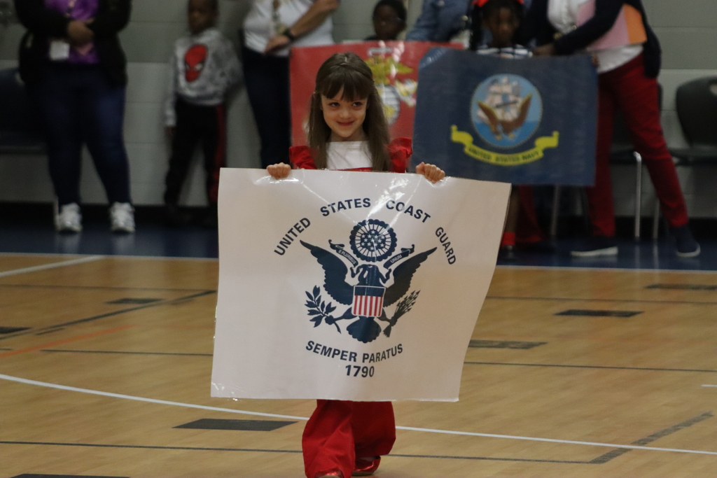A young girl holds a large U.S. Coast Guard flag banner while walking in the JWP gym