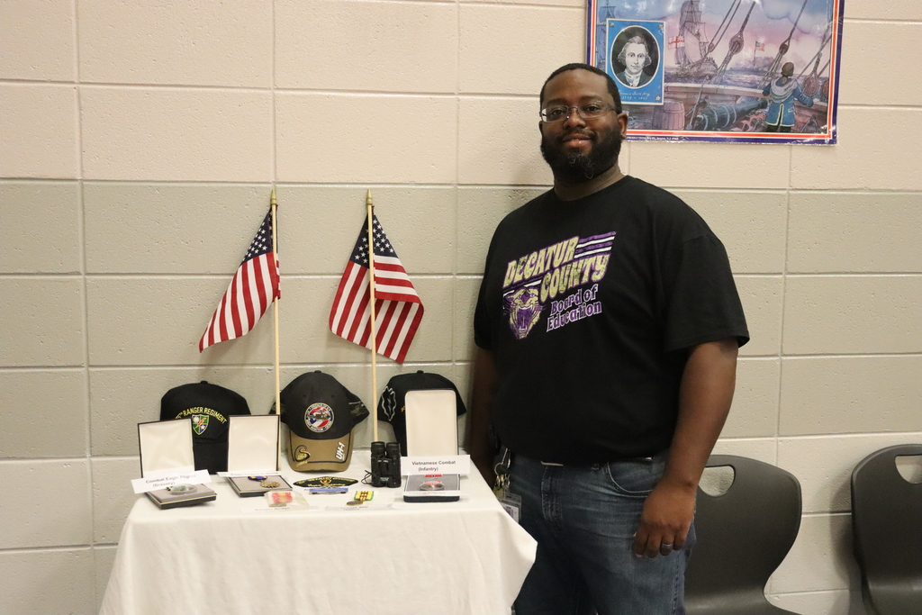 A man stands beside a display table with American flags, military caps, and medals.