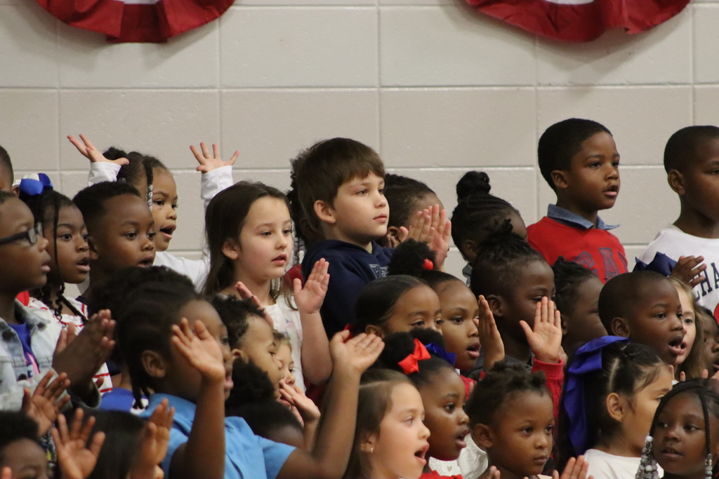 Kindergarten students dressed in red, white, and blue sing together during the Veterans Day program.