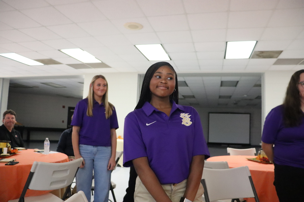 Two Bearcat Ambassador students stand during introductions at the meeting. One smiles slightly while an adult seated behind them looks on.