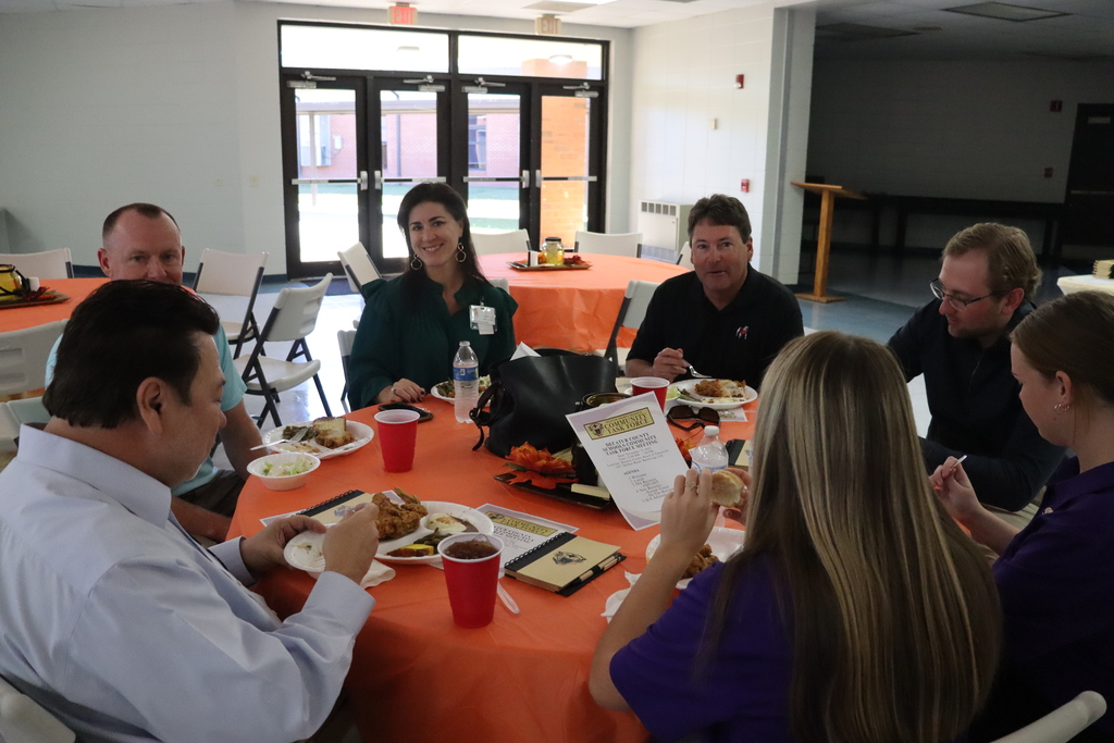Community members and Bearcat Ambassador students sit at a lunch table during the event. One person holds a red cup while another smiles toward the camera.